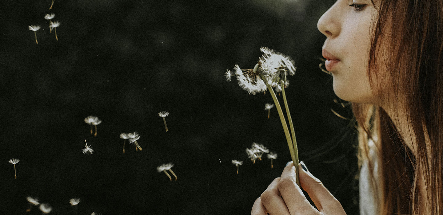 A young person blowing dandelion seeds into the dark