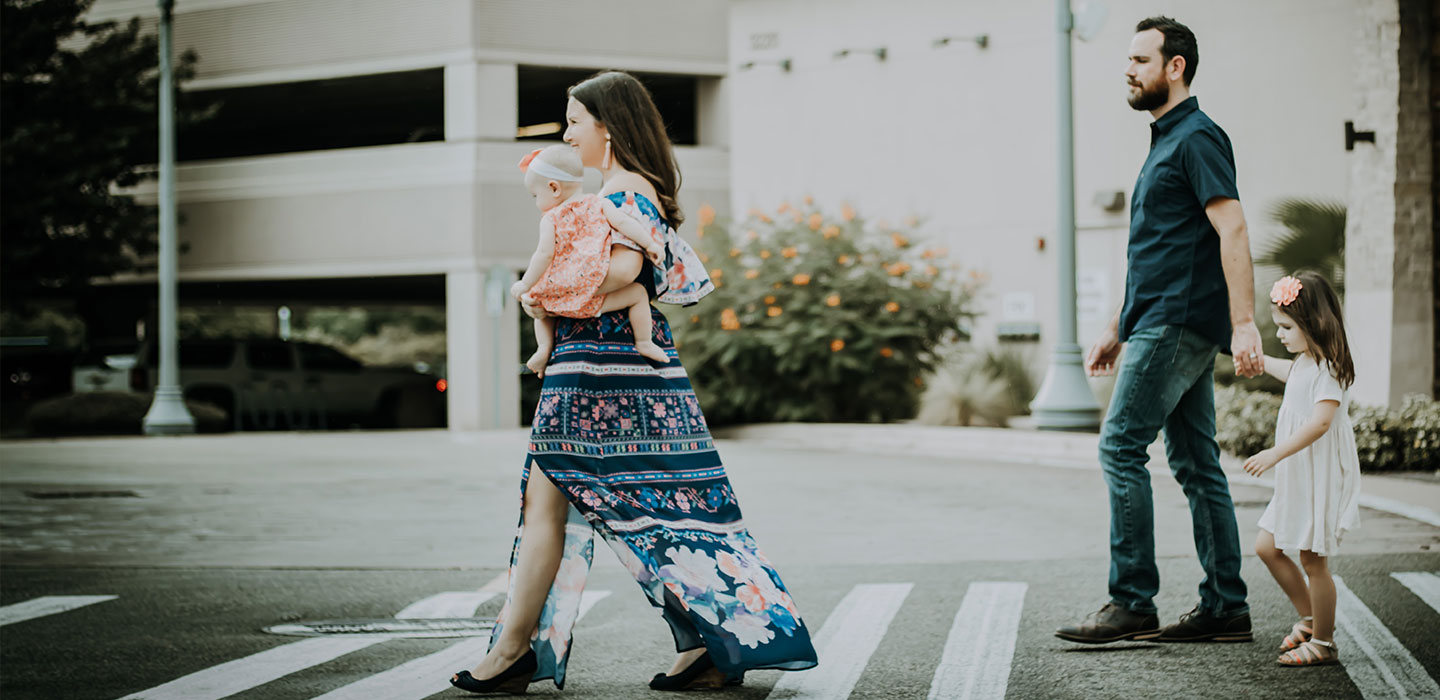 A family crossing a city street together, a parent carrying the youngest